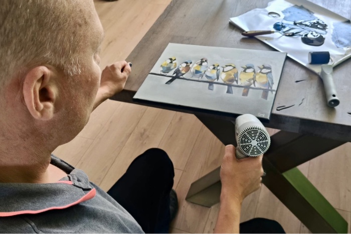 Gideon brengt de laatste afwerking aan een van zijn handgeschilderde olieverfschilderijen in zijn atelier