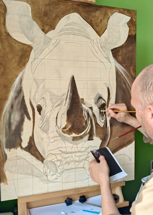 Gideon schildert met de hand een groot olieverfschilderij van een neushoorn in zijn atelier.